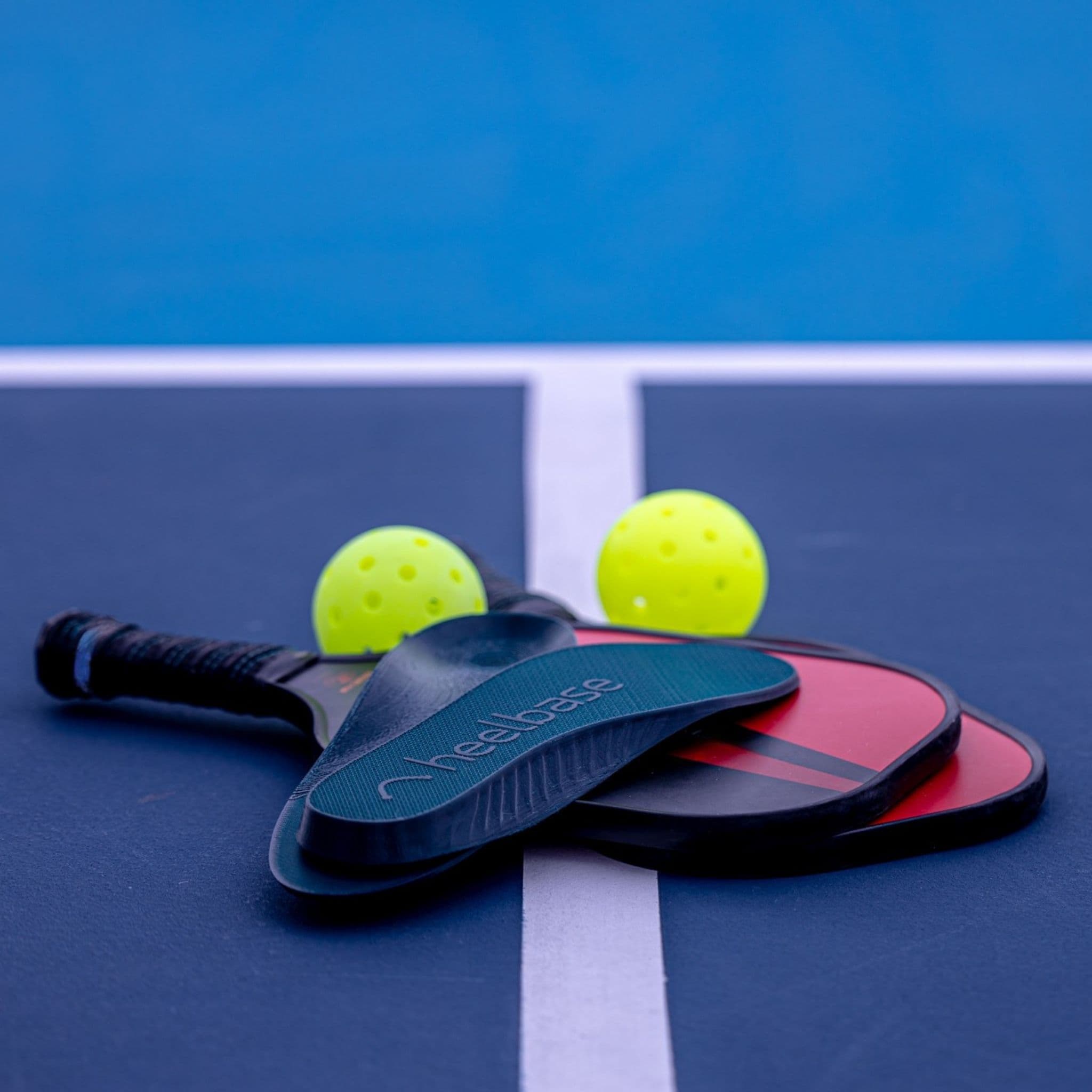 HeelBase Drive insoles shown in profile with pickleball paddles and balls on court