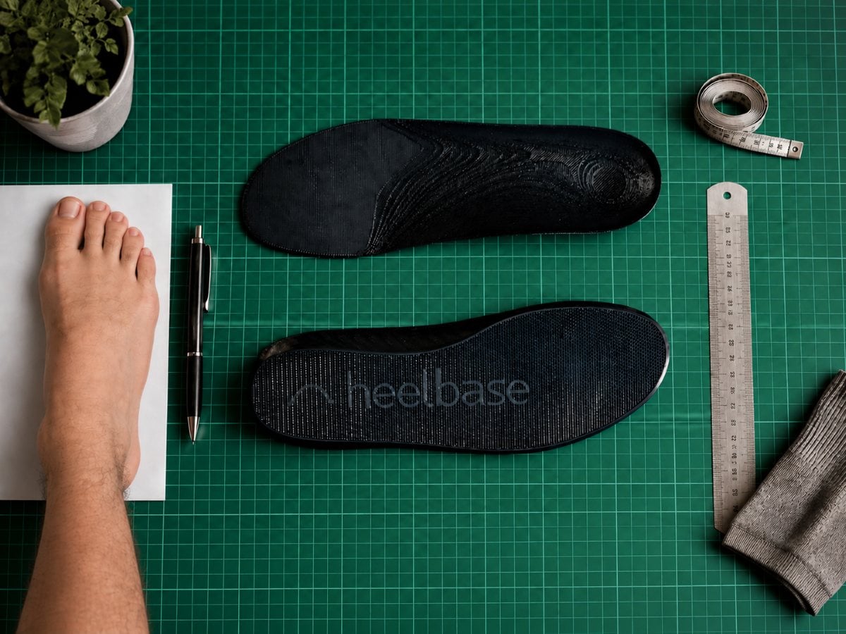 Foot, HeelBase insoles, ruler, pen, and measuring tape arranged for an insole sizing measurement