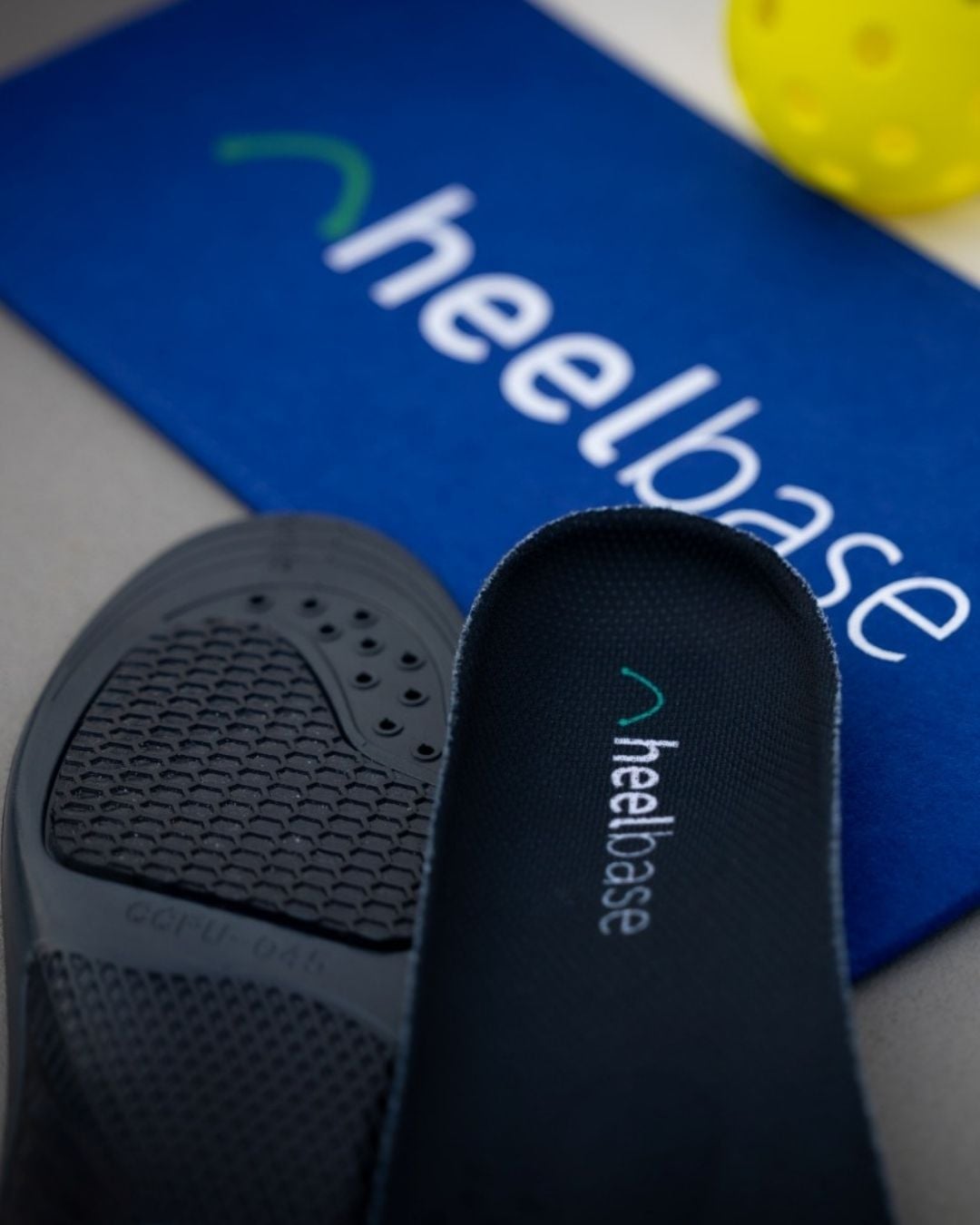 HeelBase Stance insoles beside a pickleball and HeelBase court towel